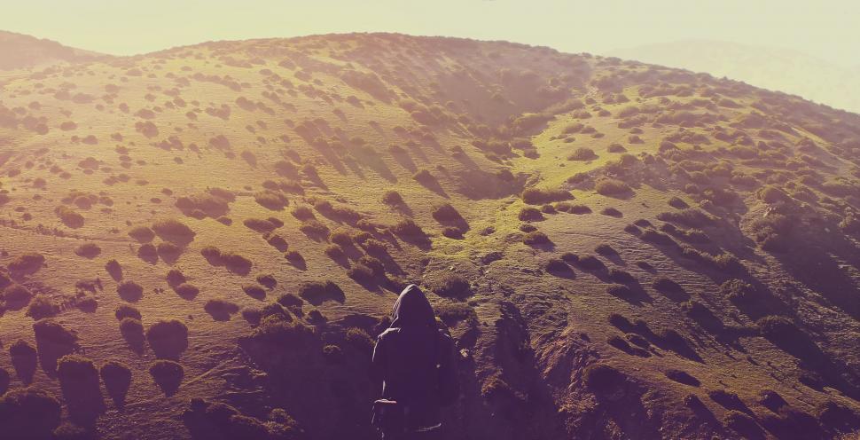 Free Image of Lone figure on a sunlit hilly terrain 