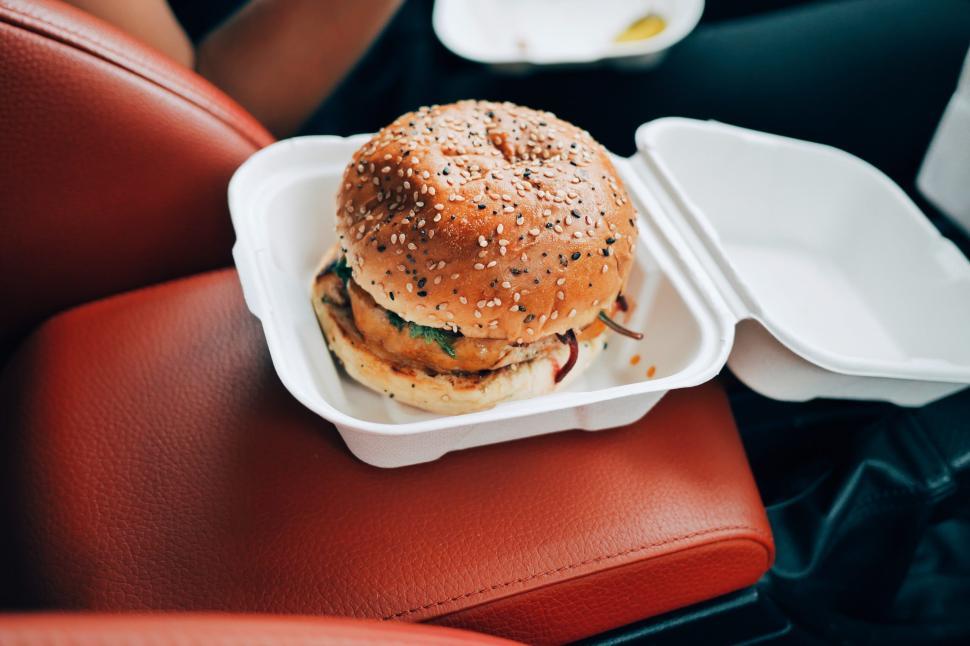 Free Image of Juicy burger in a takeaway container on car seat 