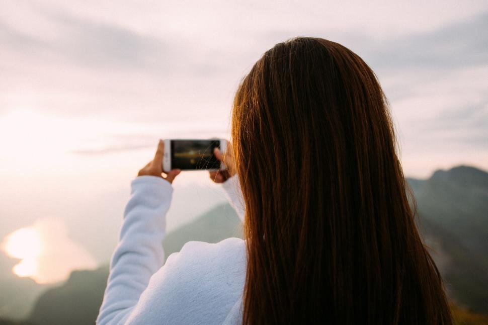 Free Image of Woman capturing sunset on smartphone at picturesque location 