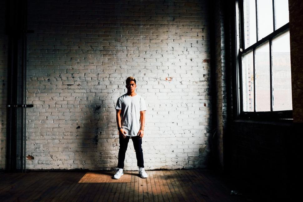 Free Image of Young man standing against a white brick wall 