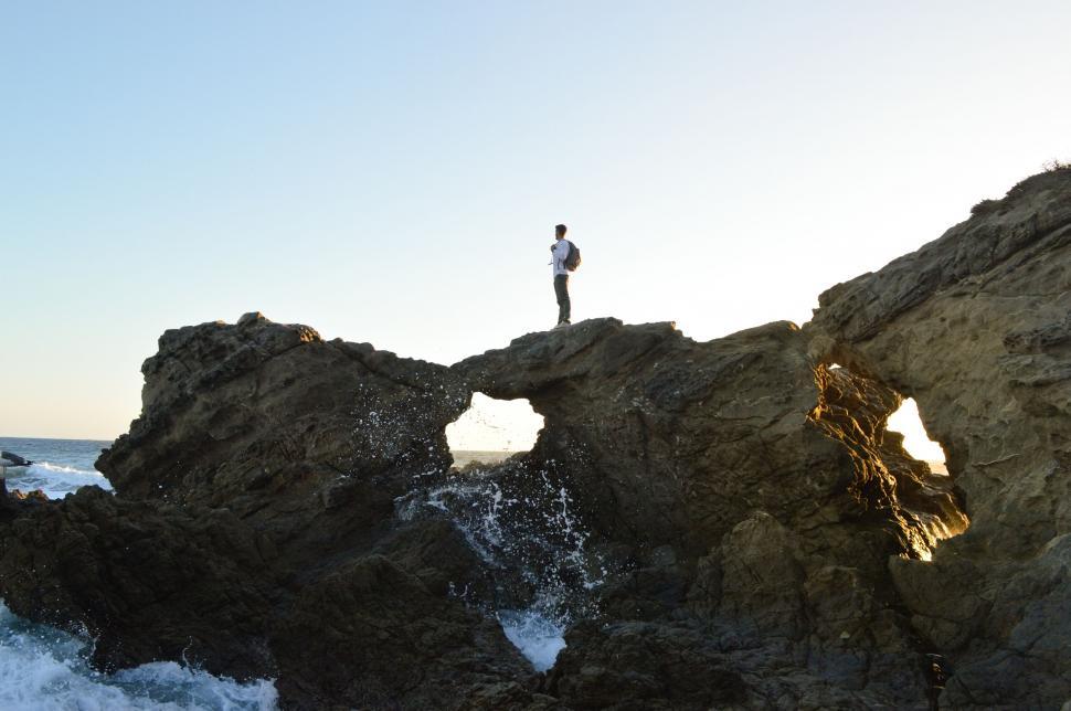 Free Image of Man standing on rocky arch by the sea 