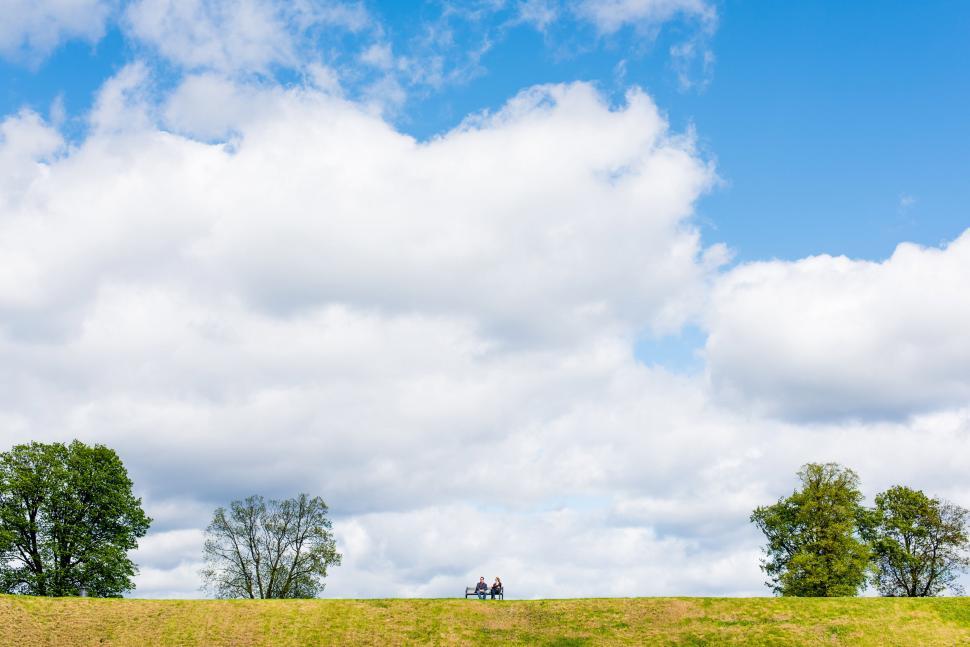 Free Image of Couple sitting on a hill under expansive sky 