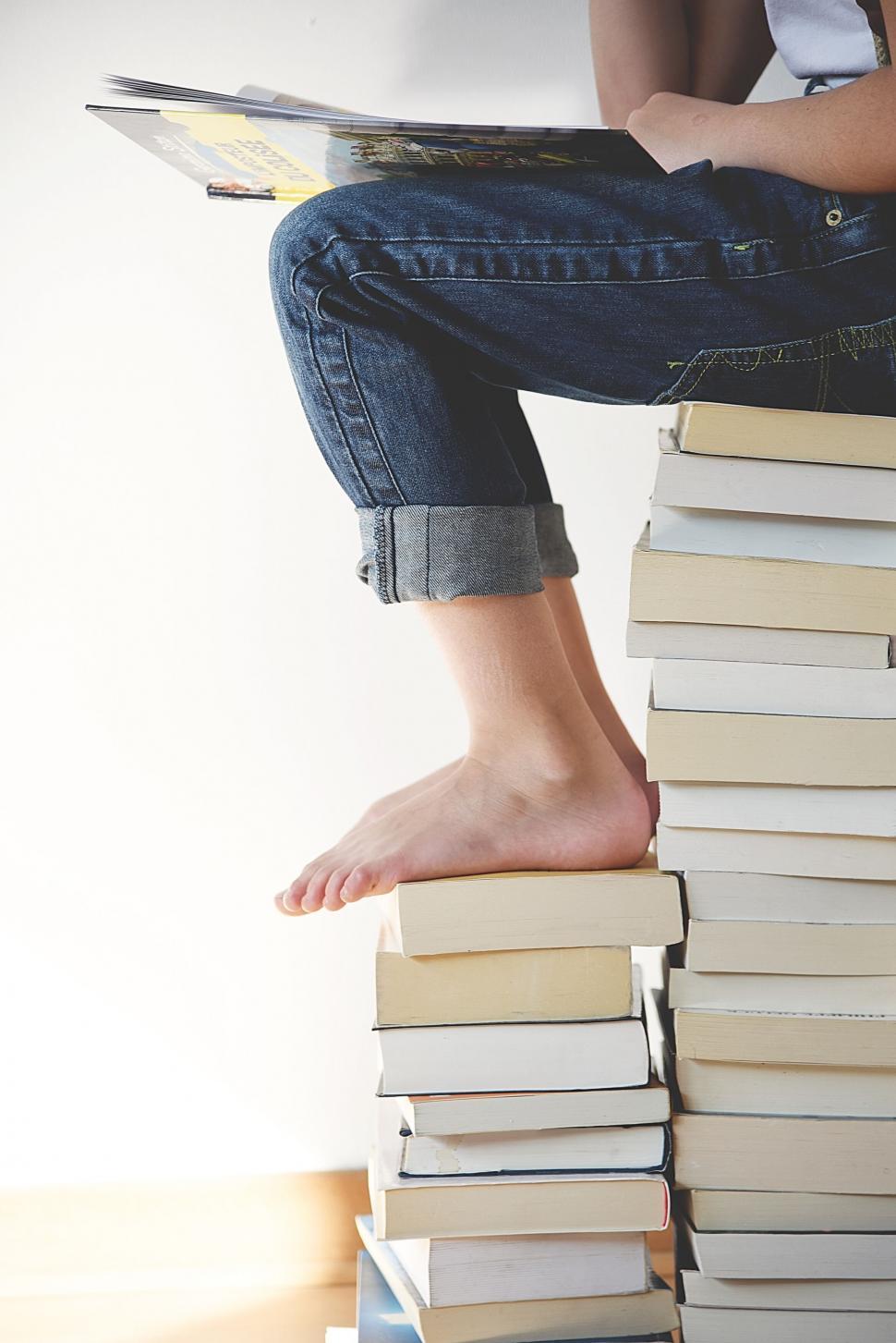 Free Image of Person reading a book on top of book pile 