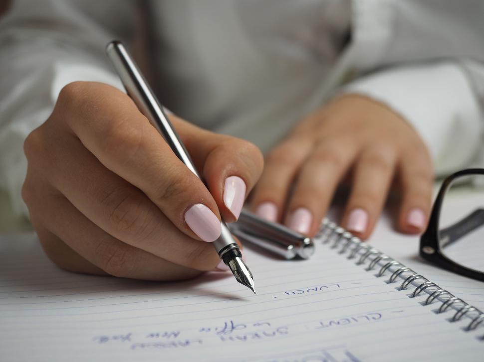 Free Image of Hand writing in notebook with pen, glasses nearby 