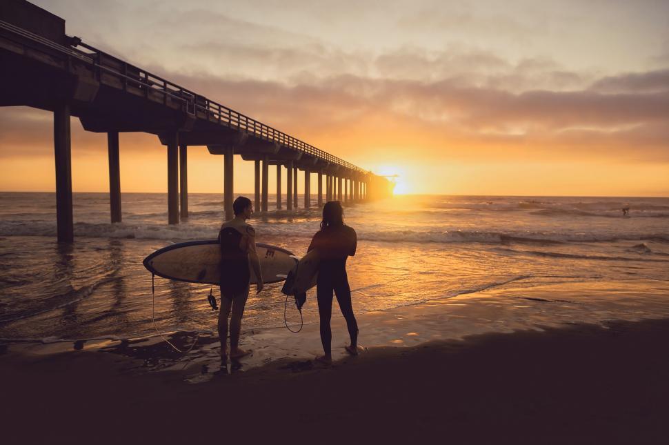 Free Image of Surfers walking on beach at sunset 