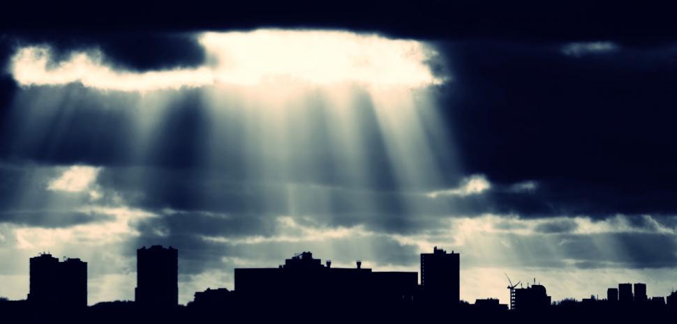 Free Image of Dramatic sunbeams through clouds over city 