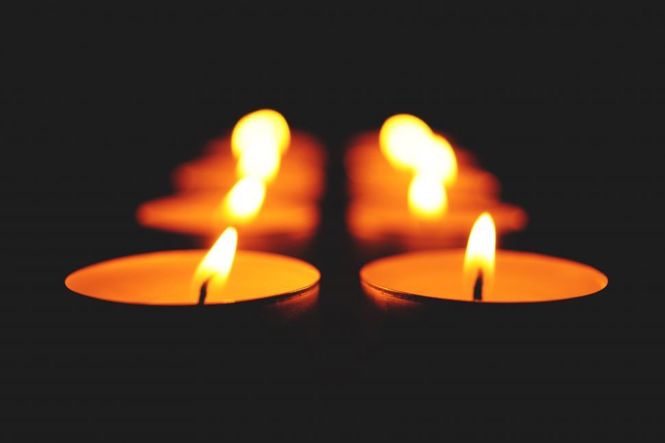 Free Image of Four lit tea light candles on dark backdrop 