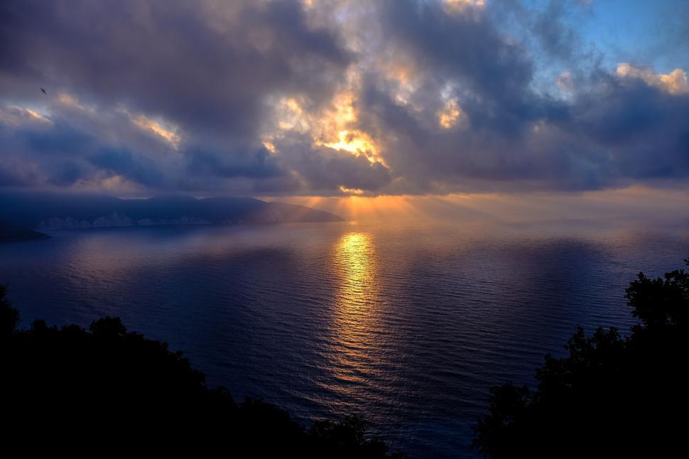 Free Image of Sunset over a calm sea with cloud breaks 