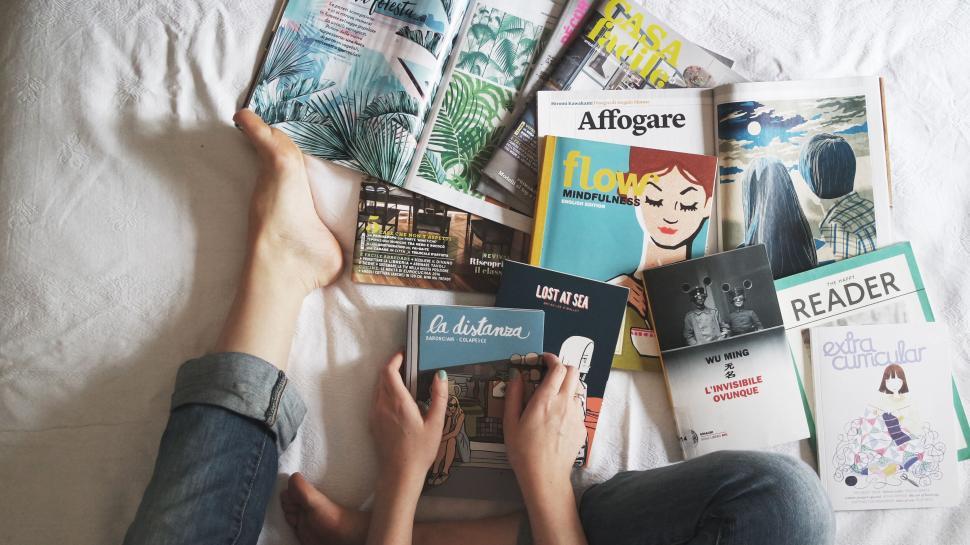 Free Image of Person reading amidst scattered magazines 