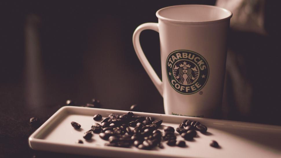 Free Image of Starbucks cup and coffee beans against dark backdrop 