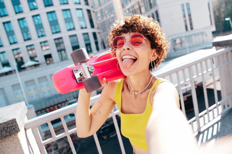 Free Image of A woman with short curly hair wearing sunglasses and holding a skateboard 