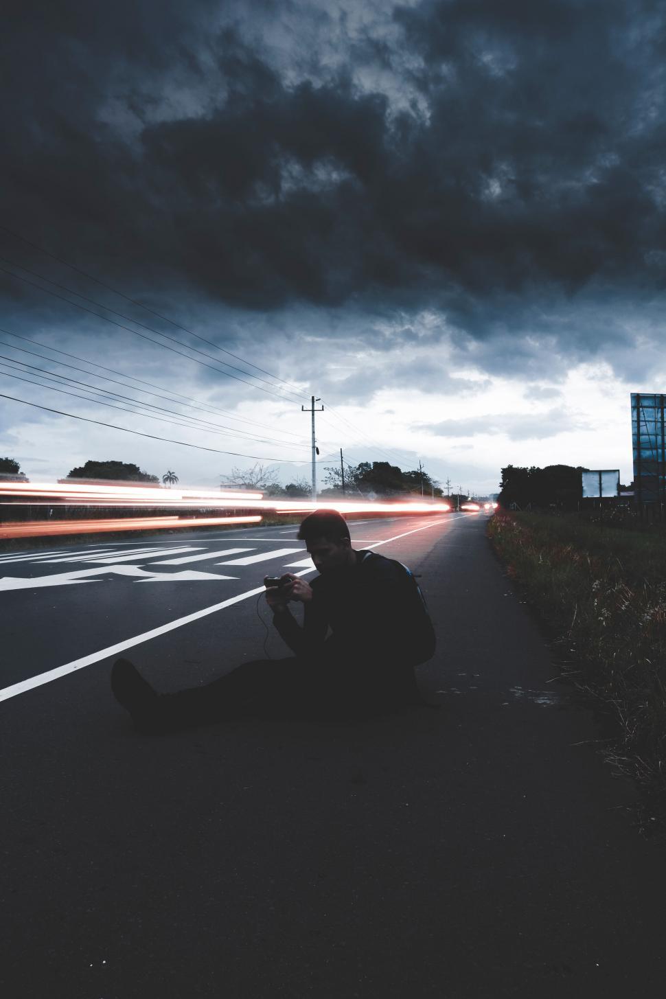 Free Image of Person sitting on road with light trails 