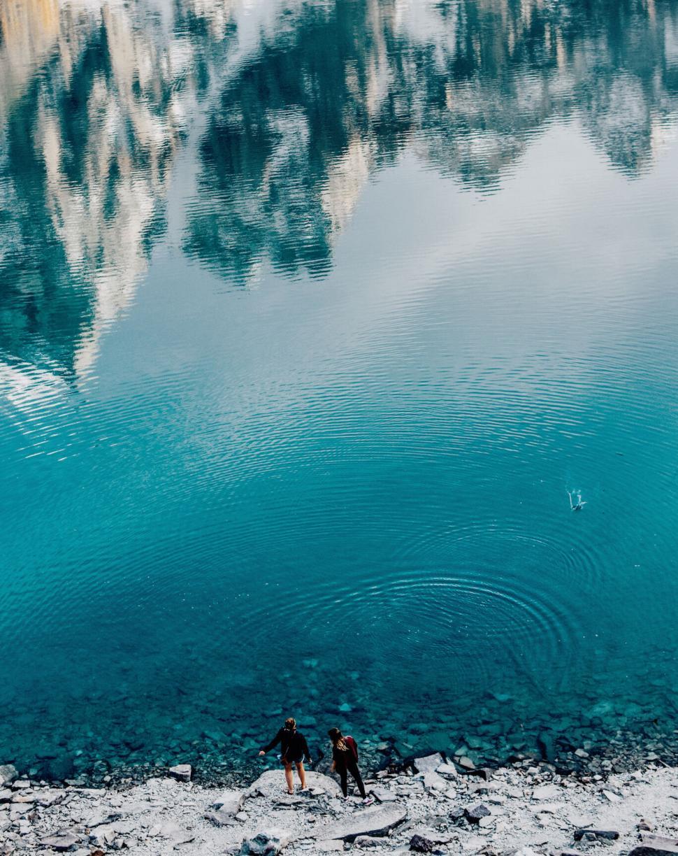 Free Image of Two people by a turquoise mountain lake 