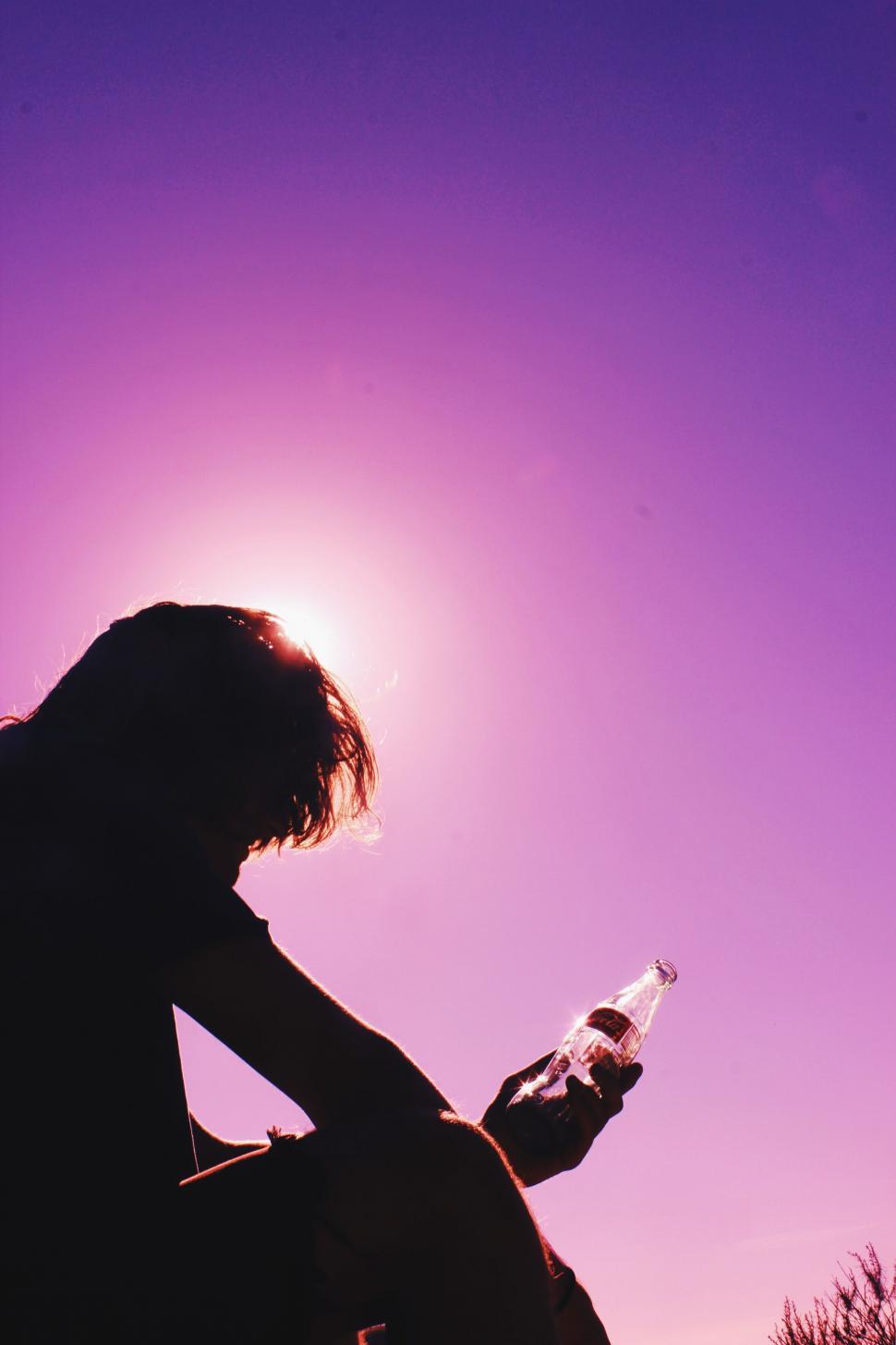 Free Image of Silhouette of person with a bottle against sun 