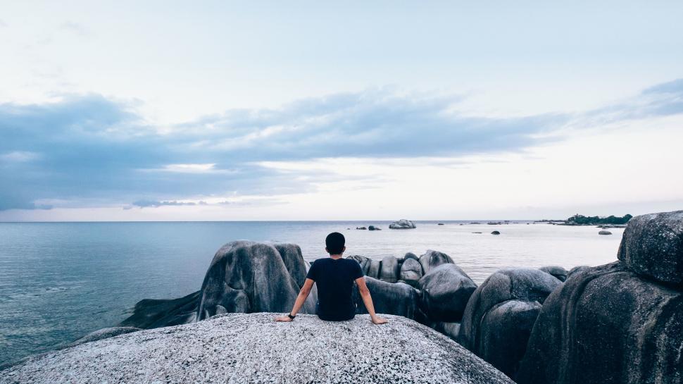 Free Image of Man sitting on boulder by calm sea 