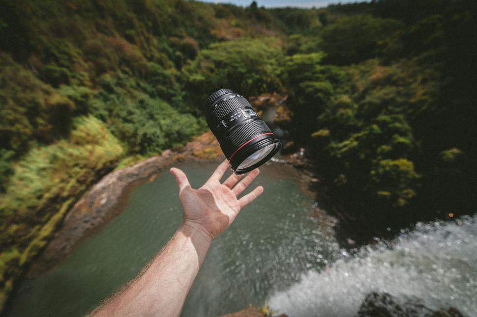 Free Image of Camera lens tossed in the air near a waterfall 