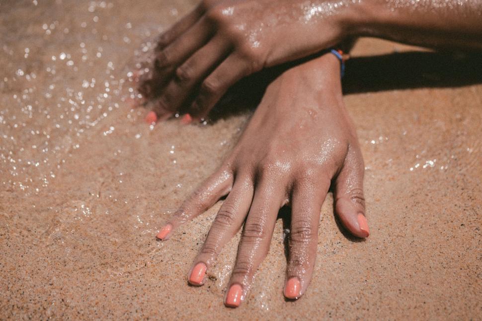 Free Image of Hand with coral nail polish on beach sand 