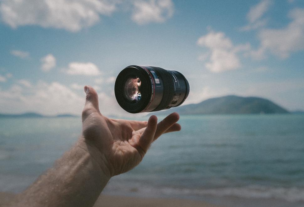 Free Image of Camera lens floating above hand at beach 