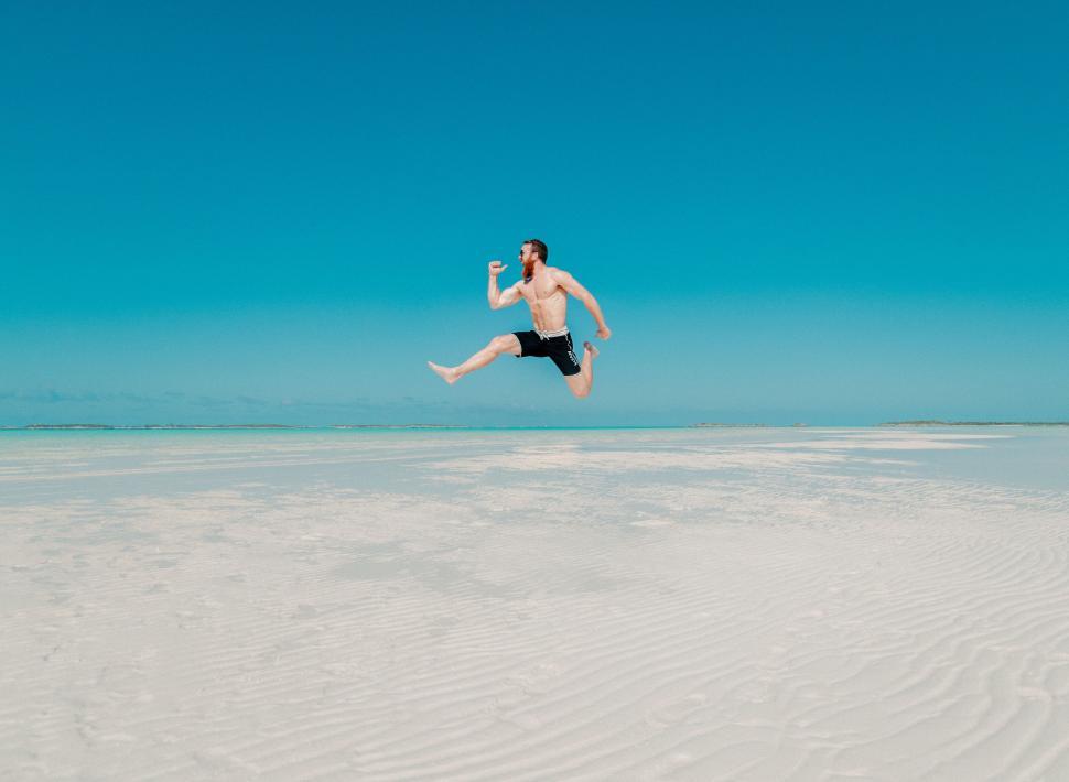 Free Image of Man jumping over deserted white sands 