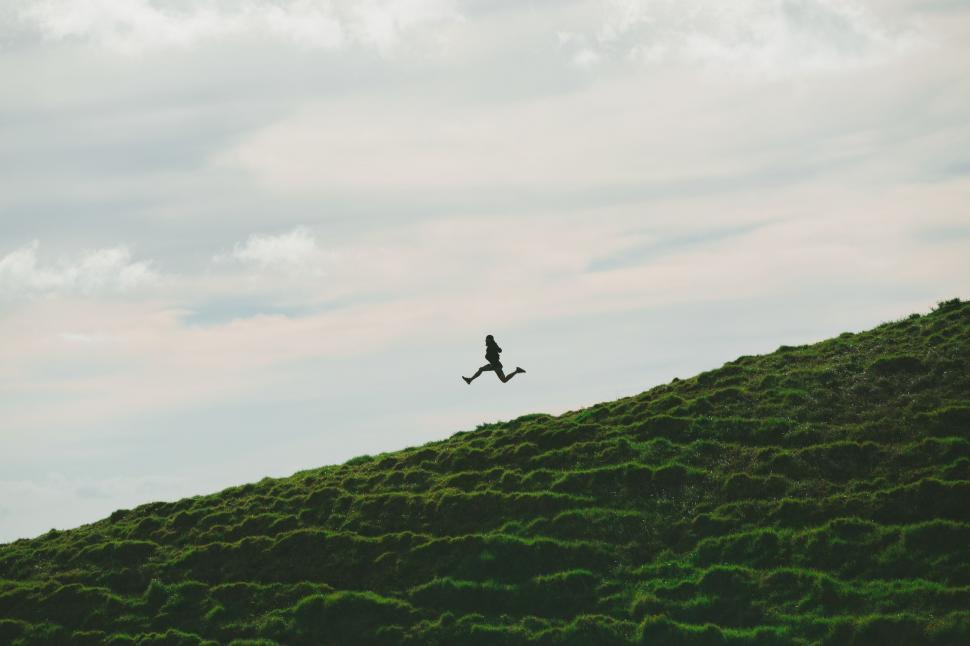 Free Image of Silhouette of person jumping on hill at dusk 