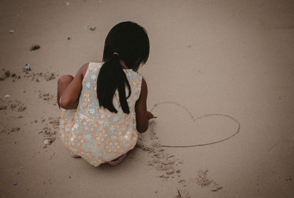 Free Image of Young girl drawing heart shape in the sand 