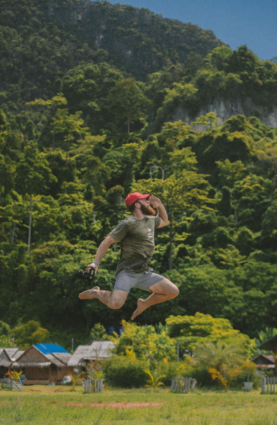 Free Image of Man jumping with a camera in natural scenery 