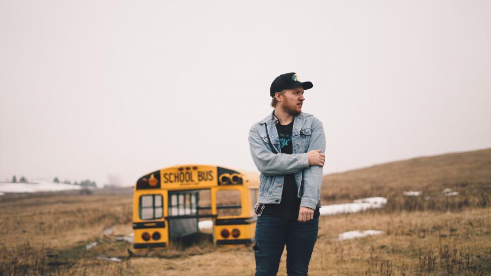 Free Image of Man leaning on a school bus in a field 