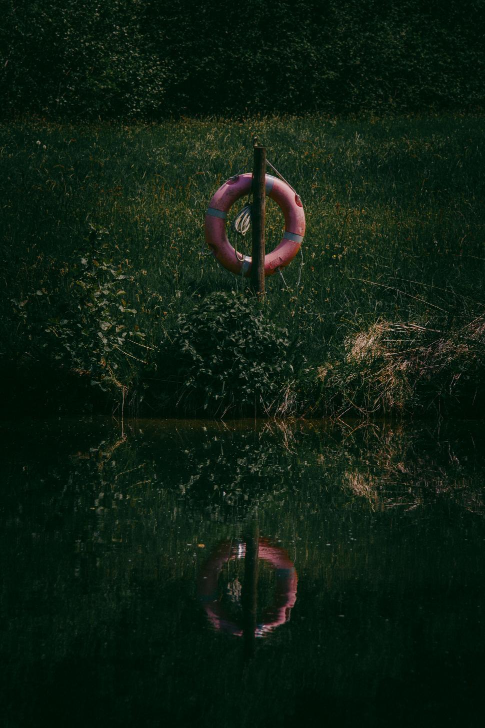 Free Image of Lifebuoy on pole reflected in dark water 