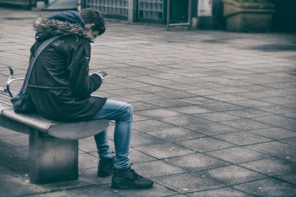 Free Image of Person sitting on bench using smartphone 