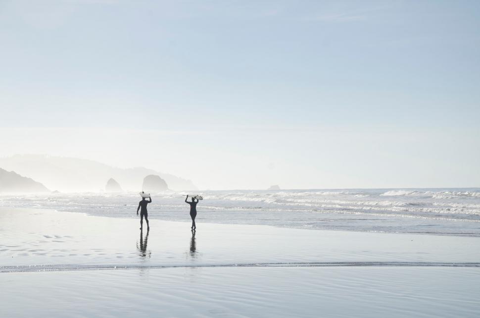 Free Image of Two people walking on a misty beach 