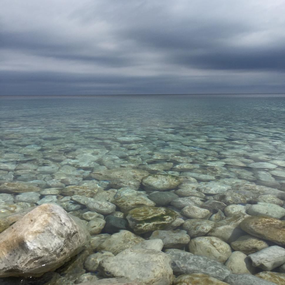 Free Image of Clear lake with pebbles and overcast sky 