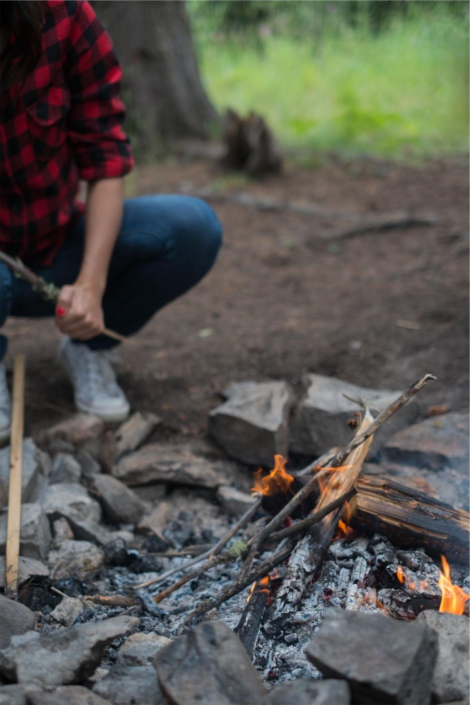 Free Image of Person squatting by a campfire in the woods 