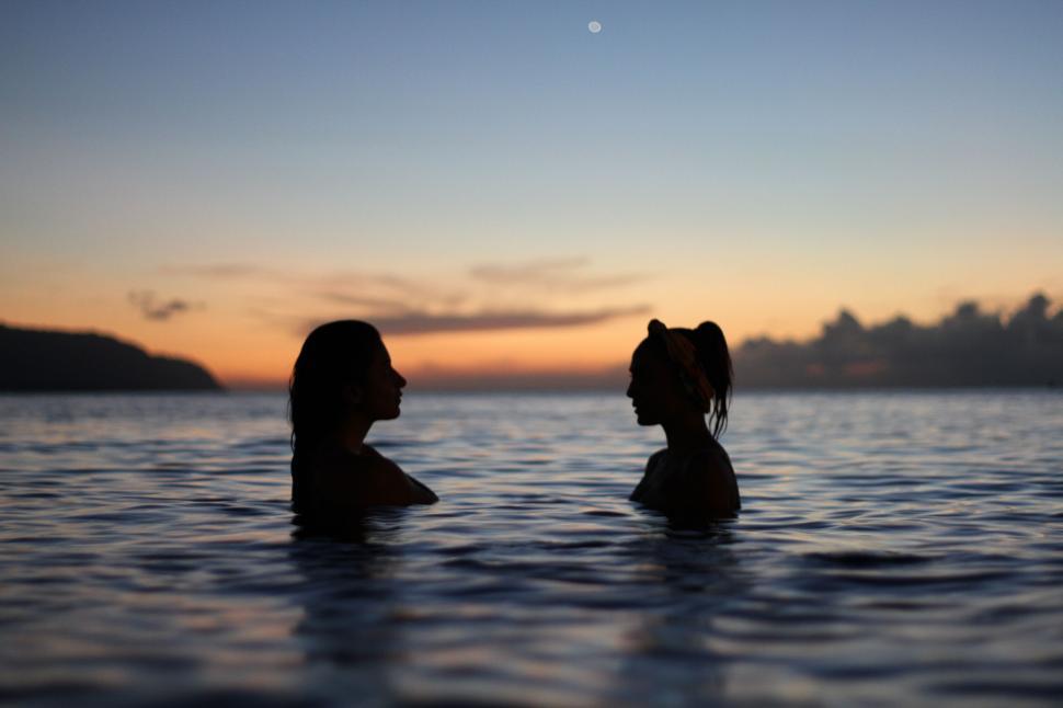 Free Image of Silhouettes of two people in water at dusk 