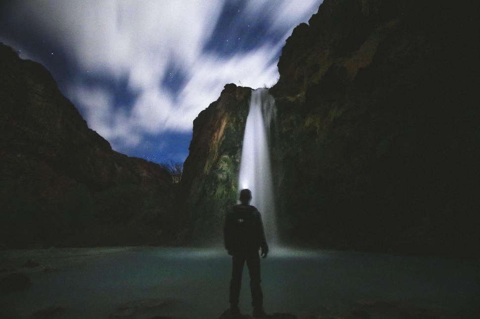 Free Image of Person silhouetted against waterfall at night 