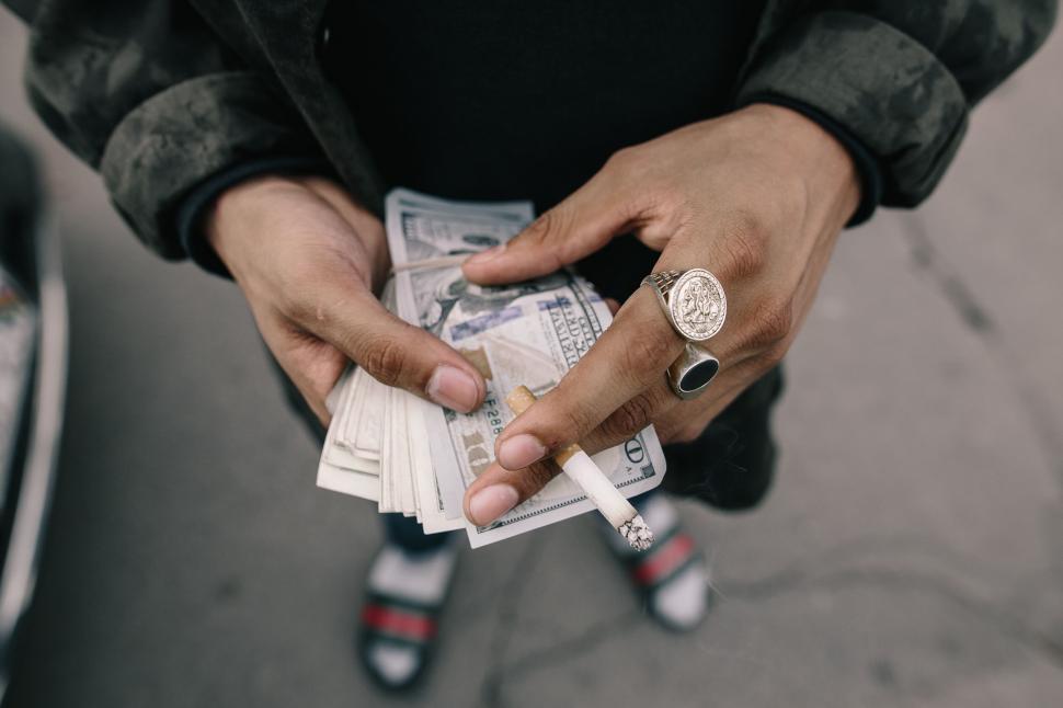 Free Image of Person holding cash and a lit cigarette 