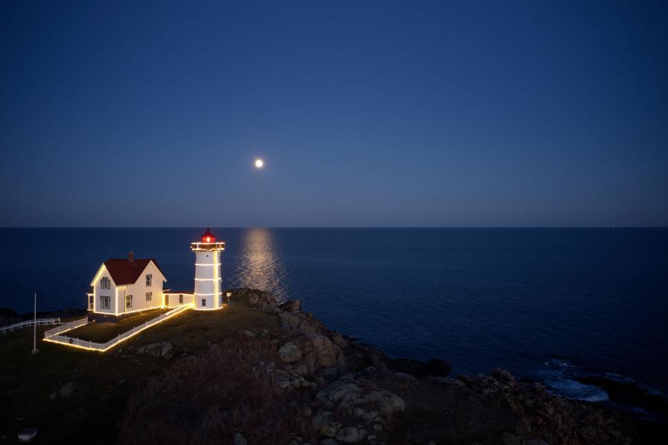 Free Image of Lit-up lighthouse standing on rocky coast in moonlight 