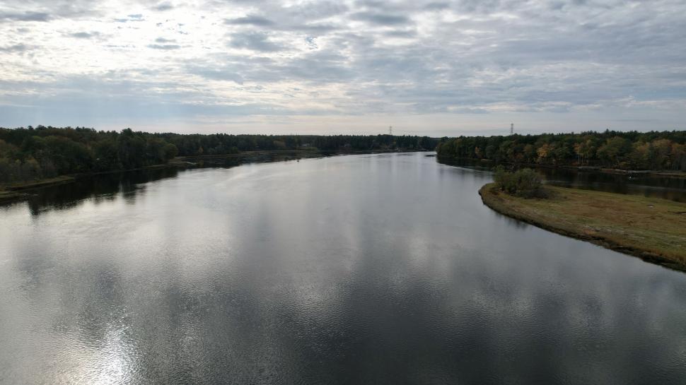 Free Image of Wide river with tree-lined banks under an overcast sky 