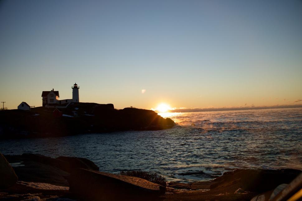 Free Image of Dramatic sunrise with lighthouse by rocky ocean shore 