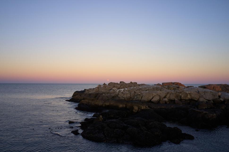 Free Image of Rocky coastal sunset with a tranquil ocean horizon 