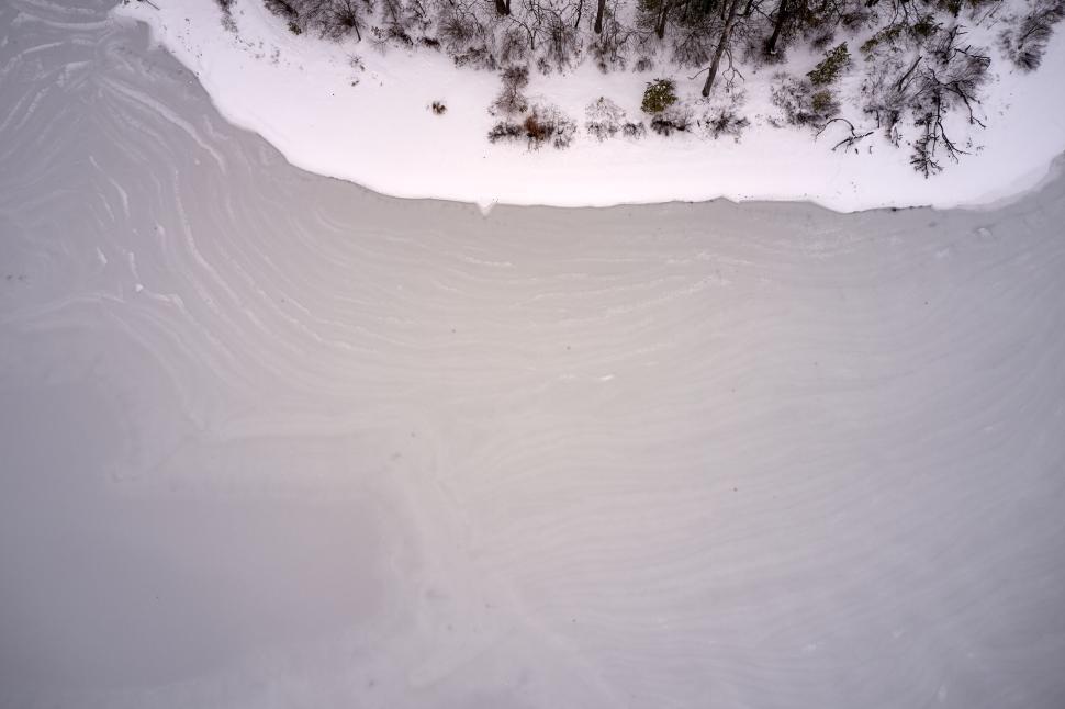 Free Image of Frozen lake surface with snow-covered shore aerial view 