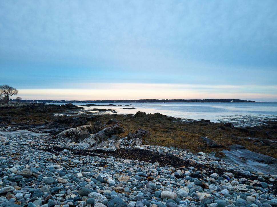 Free Image of Rocky shore at dusk, with calm sea and overcast sky 