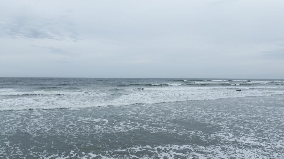 Free Image of Calm waves gently lapping against the shore, overcast day 