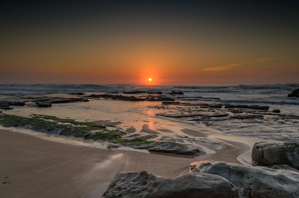 Free Image of Sunset over a beach with smooth rocks and calm waves. 