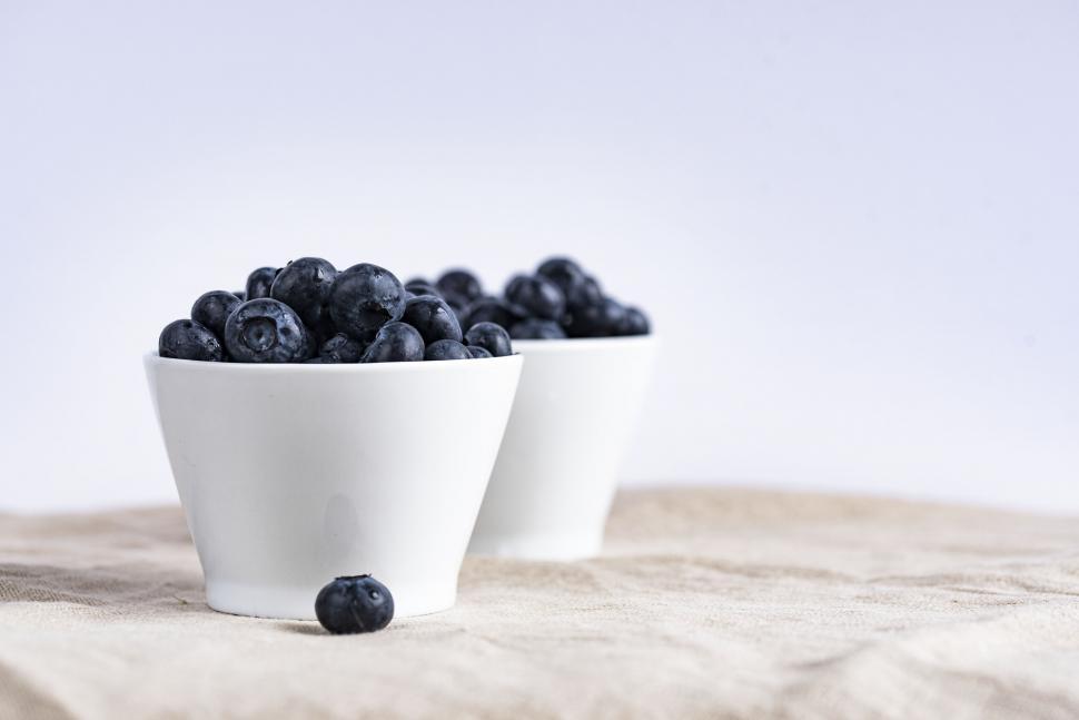 Free Image of Two white cups filled with fresh blueberries on linen cloth 