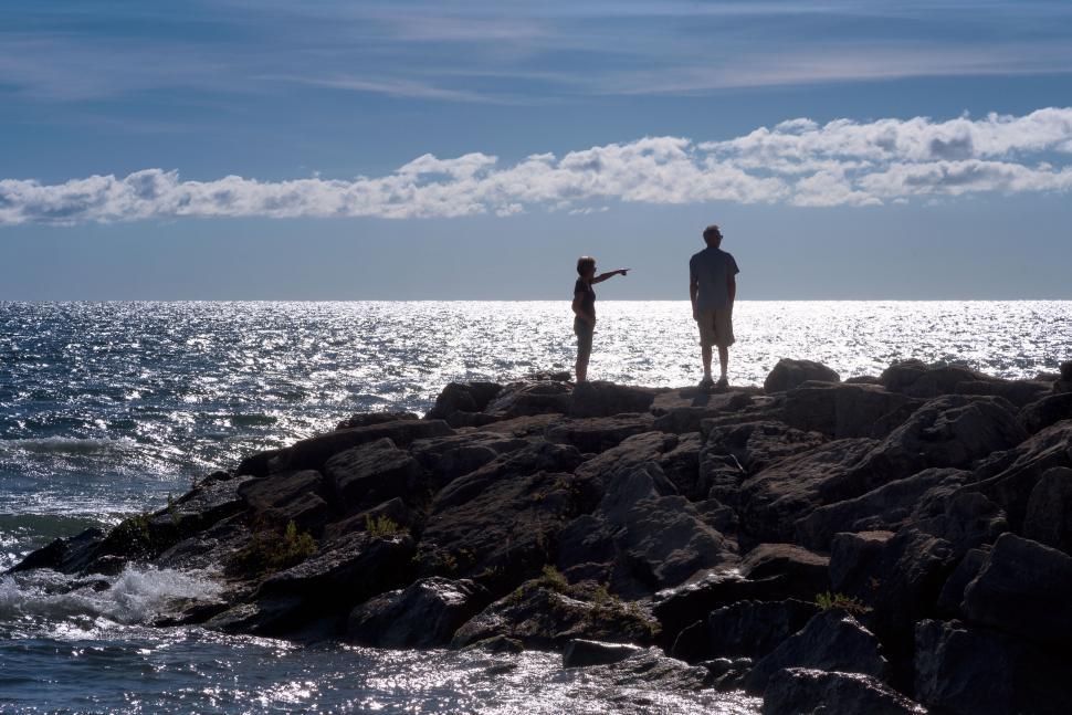 Free Image of Silhouetted Figures on Rocky Shore Against Bright Horizon 