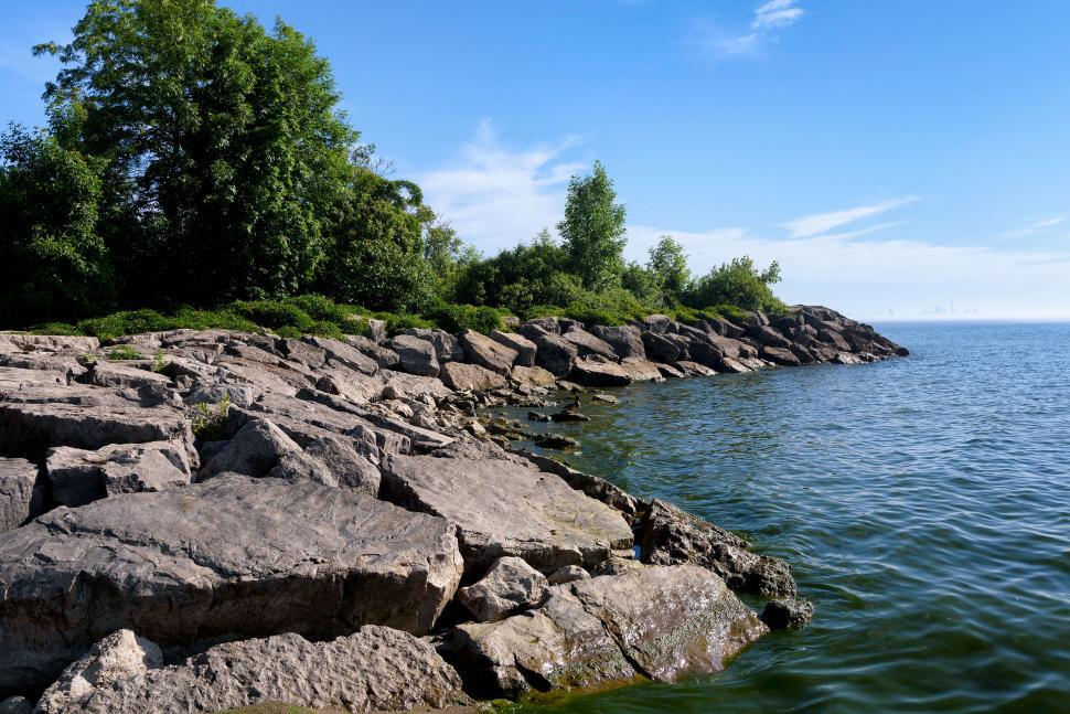 Free Image of Rocky shore meets gentle green water under clear blue sky. 