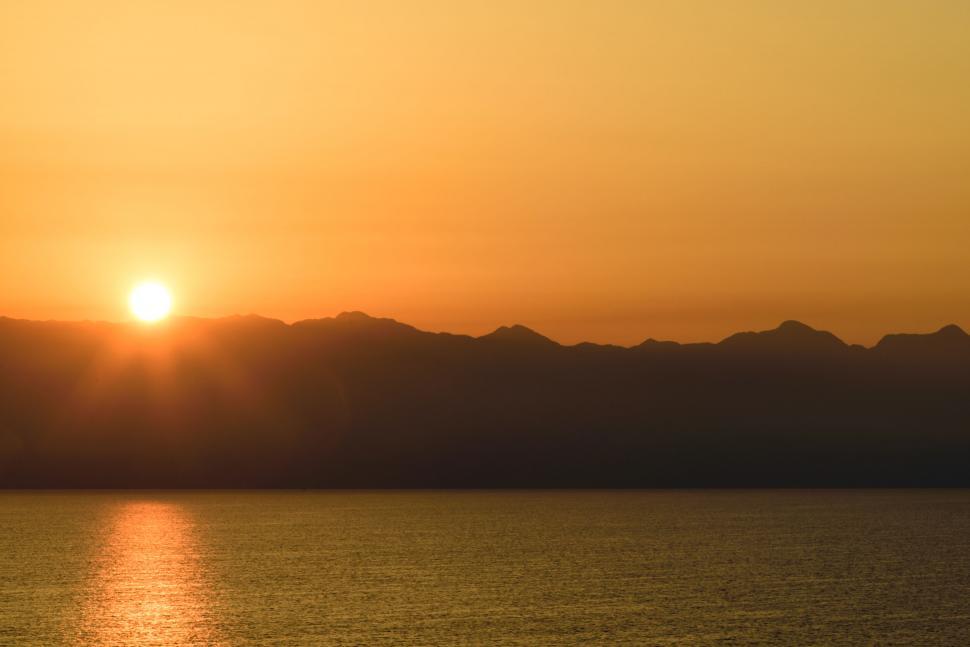 Free Image of Golden sun setting behind mountains reflecting on the sea 