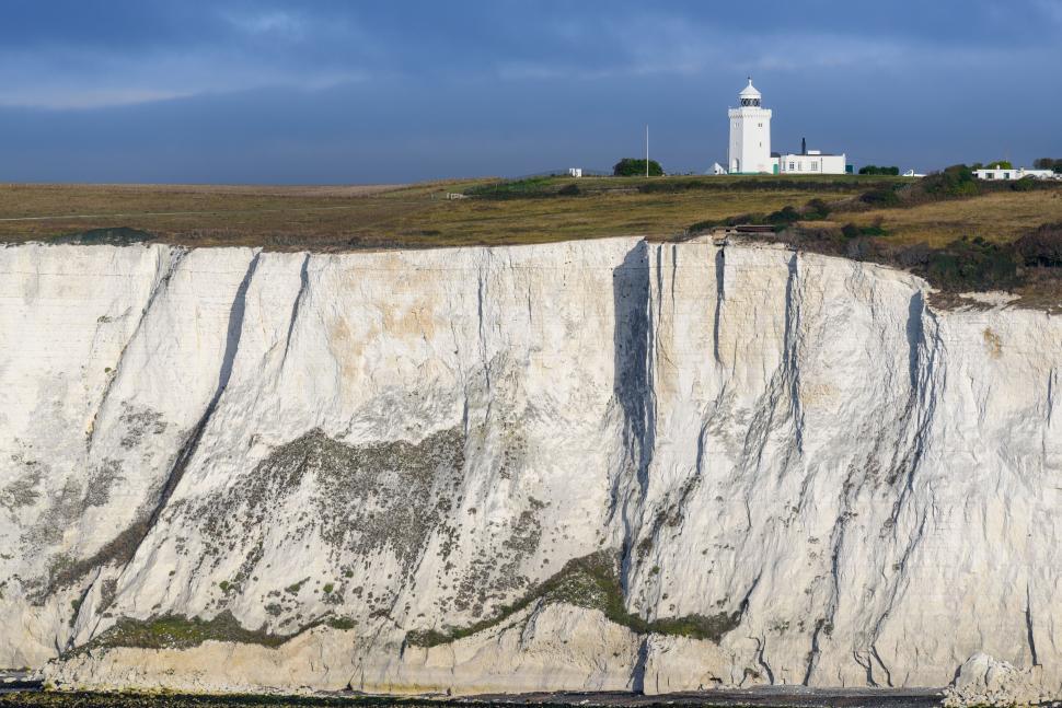 Free Image of Lighthouse perched on white cliffs with blue sky above. 