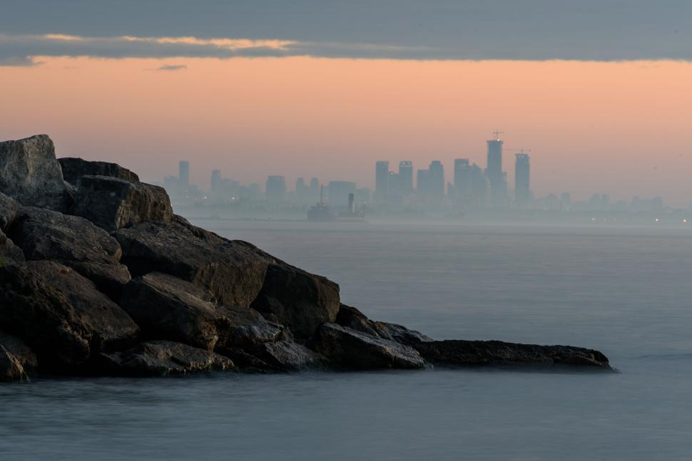 Free Image of Rocky shore with distant city skyline at sunset time. 