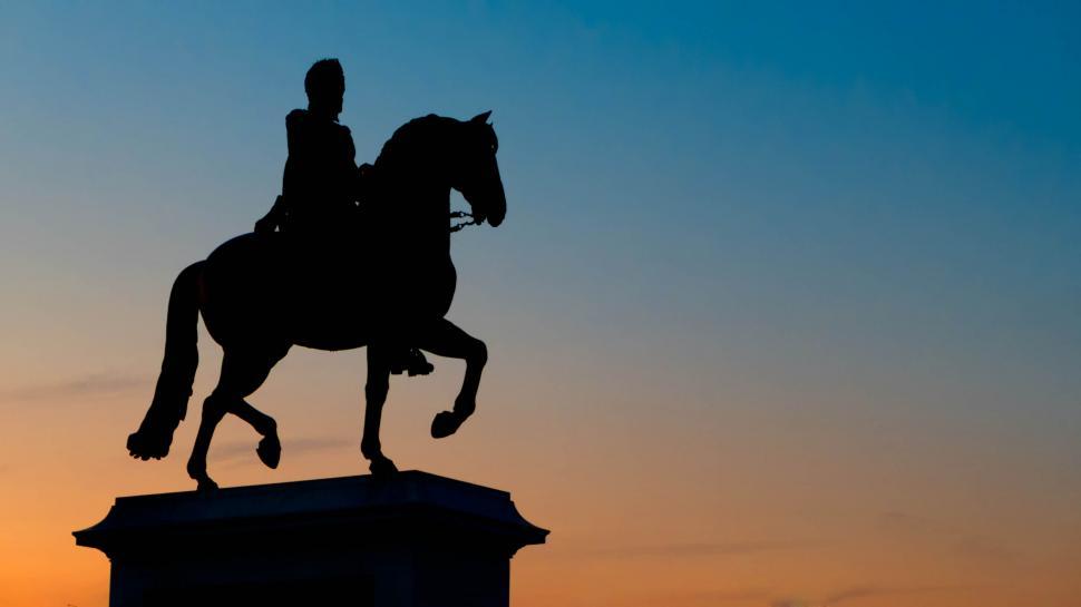 Free Image of Silhouette of a horse rider statue against a sunset sky 